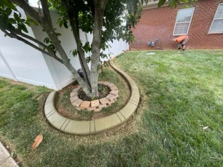 Beautiful decorative concrete curbs surrounding a tree against a white picket fence.